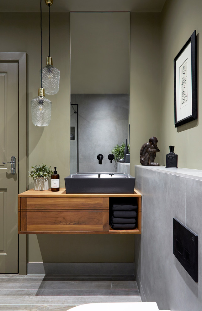 This is an example of an asian bathroom in London with flat-panel cabinets, medium wood cabinets, a one-piece toilet, gray tile, green walls, a vessel sink, wood benchtops, grey floor and brown benchtops.