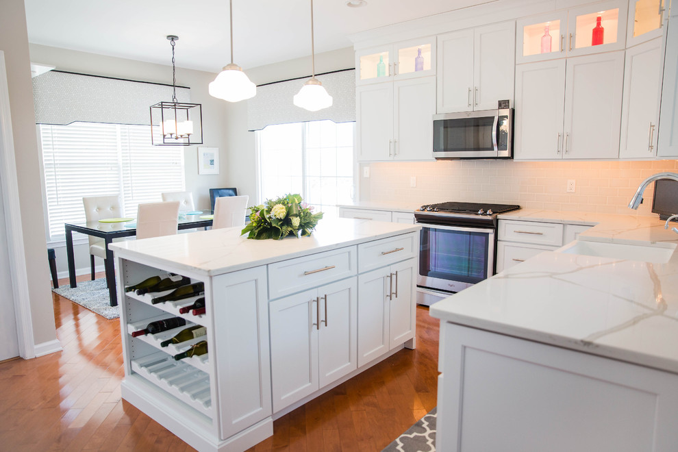 Mid-sized transitional l-shaped medium tone wood floor eat-in kitchen photo in Philadelphia with a farmhouse sink, shaker cabinets, white cabinets, quartz countertops, gray backsplash, ceramic backsplash, stainless steel appliances and an island