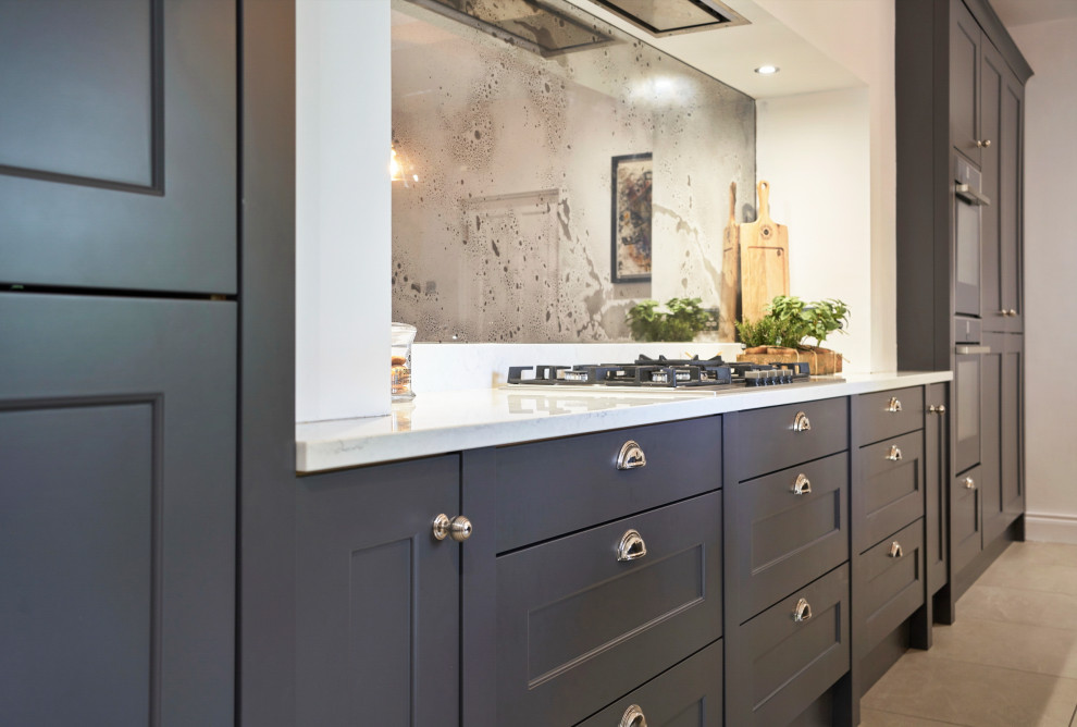 Design ideas for a mid-sized traditional galley eat-in kitchen in Belfast with a farmhouse sink, shaker cabinets, grey cabinets, quartzite benchtops, metallic splashback, glass sheet splashback, black appliances, ceramic floors, with island, beige floor and yellow benchtop.
