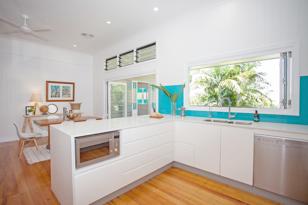 Design ideas for a mid-sized tropical u-shaped eat-in kitchen with an undermount sink, flat-panel cabinets, grey cabinets, quartz benchtops, blue splashback, glass sheet splashback, stainless steel appliances, medium hardwood floors and a peninsula.