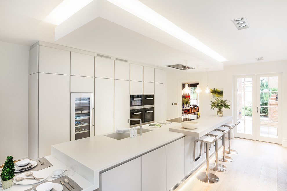 Design ideas for a large contemporary galley eat-in kitchen in Other with a double-bowl sink, flat-panel cabinets, white cabinets, solid surface benchtops, black appliances, light hardwood floors and with island.