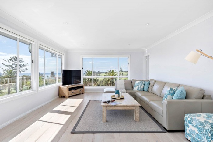 Photo of a large beach style open concept family room in Sydney with grey walls, light hardwood floors, a corner tv and multi-coloured floor.
