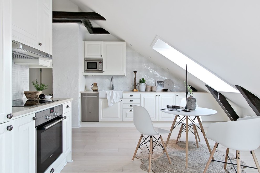 Photo of a mid-sized scandinavian l-shaped separate kitchen in Other with white cabinets, white splashback, mosaic tile splashback, stainless steel appliances, no island, beige floor, a farmhouse sink, raised-panel cabinets, light hardwood floors and grey benchtop.