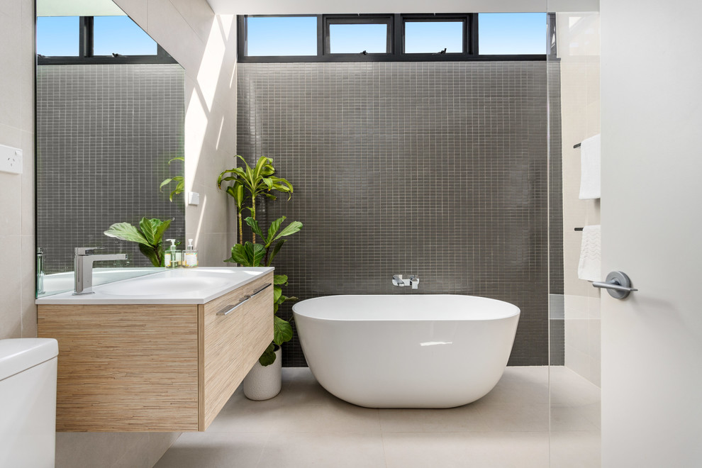 This is an example of a mid-sized contemporary master bathroom in Sydney with flat-panel cabinets, light wood cabinets, a freestanding tub, beige walls, a wall-mount sink, white benchtops, an open shower, porcelain tile, porcelain floors, beige floor and an open shower.