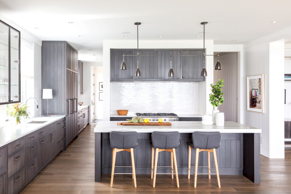 This is an example of a beach style l-shaped kitchen in Minneapolis with an undermount sink, flat-panel cabinets, grey cabinets, white splashback, stainless steel appliances, medium hardwood floors, with island, brown floor and white benchtop.