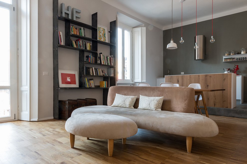 Mid-sized contemporary loft-style living room in Milan with a library, grey walls, light hardwood floors and a freestanding tv.