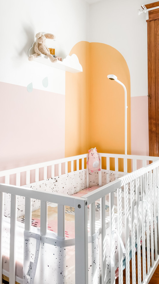 Inspiration for a small scandinavian nursery for girls in Boston with pink walls and light hardwood flooring.