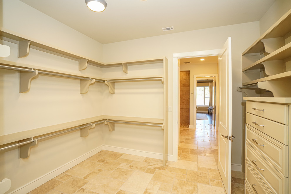 Mid-sized country gender-neutral walk-in wardrobe in Austin with raised-panel cabinets, beige cabinets, travertine floors and beige floor.