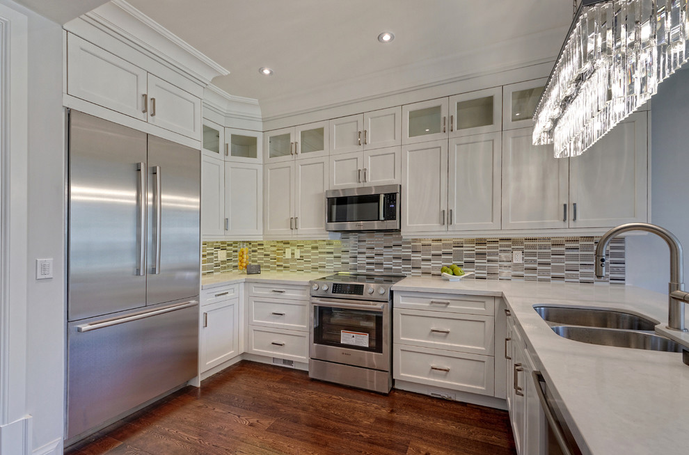 Mid-sized transitional l-shaped open plan kitchen in Toronto with a double-bowl sink, shaker cabinets, white cabinets, quartz benchtops, grey splashback, matchstick tile splashback, stainless steel appliances, dark hardwood floors, no island and brown floor.