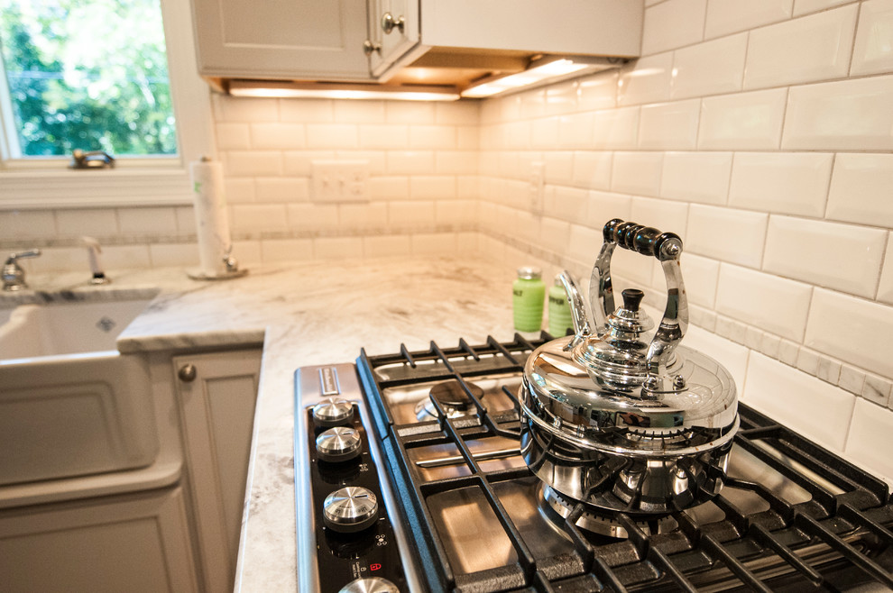 Inspiration for a small transitional u-shaped medium tone wood floor enclosed kitchen remodel in Milwaukee with a farmhouse sink, shaker cabinets, white cabinets, granite countertops, white backsplash, subway tile backsplash, stainless steel appliances and a peninsula