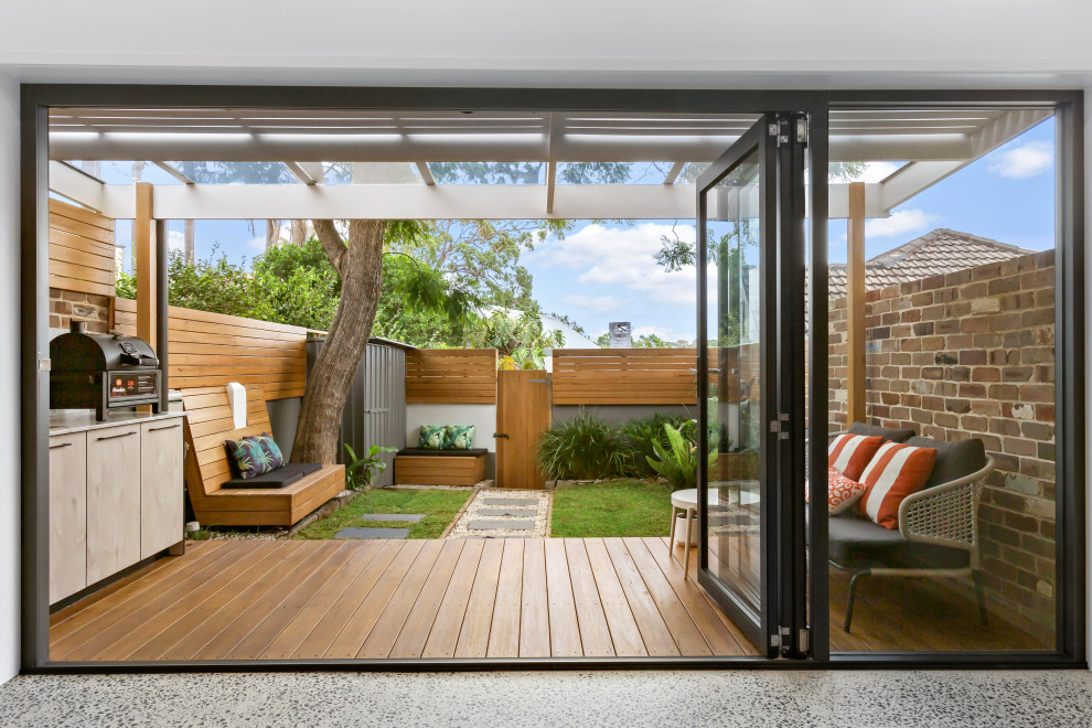 This is an example of a scandi back ground level terrace in Sydney with an outdoor kitchen and a pergola.