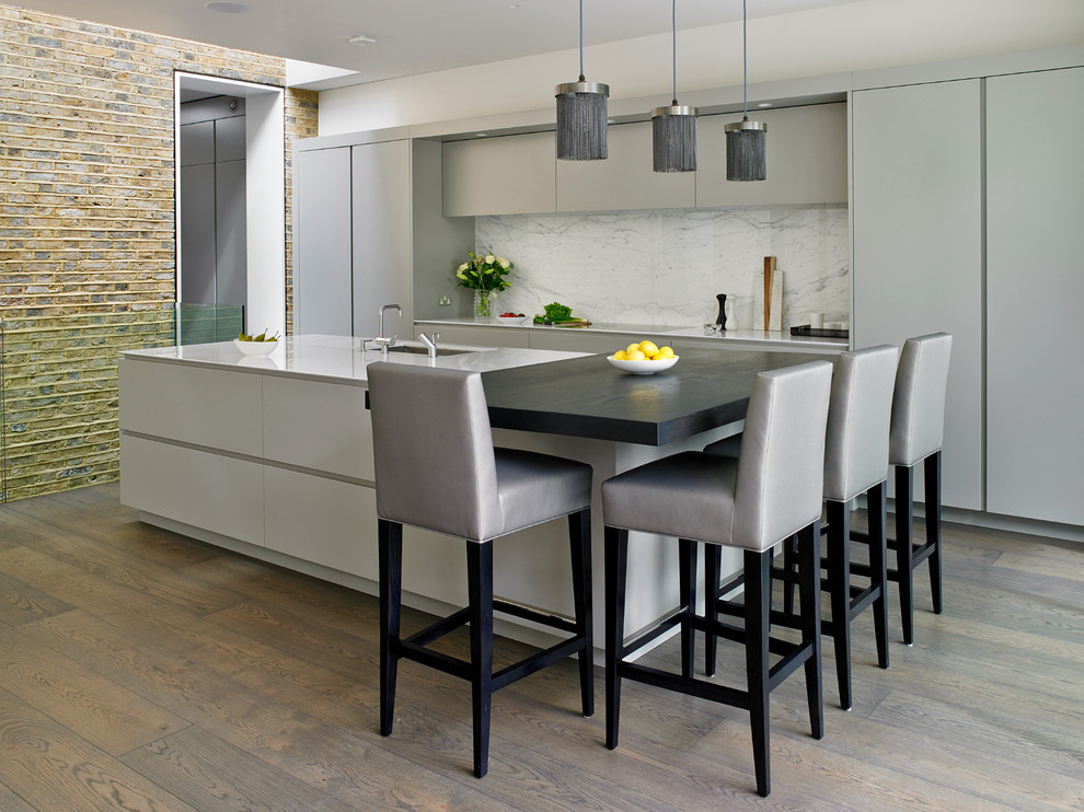 This is an example of a contemporary kitchen in London with an undermount sink, flat-panel cabinets, grey cabinets, white splashback, with island, panelled appliances and dark hardwood floors.