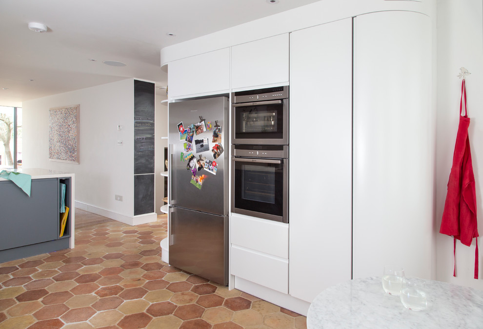 Large contemporary l-shaped eat-in kitchen in London with terra-cotta floors, a double-bowl sink, flat-panel cabinets, solid surface benchtops, white splashback, stainless steel appliances, with island, multi-coloured floor, white benchtop and white cabinets.