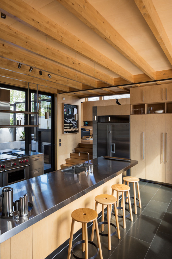 Large contemporary u-shaped eat-in kitchen in Auckland with an integrated sink, flat-panel cabinets, stainless steel cabinets, stainless steel benchtops, stainless steel appliances, slate floors and multiple islands.