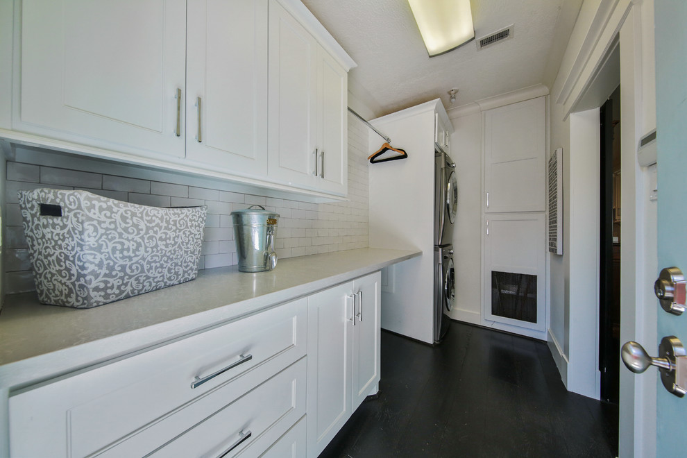 This is an example of a mid-sized transitional single-wall utility room in Houston with beaded inset cabinets, white cabinets, quartz benchtops, white walls, dark hardwood floors and a stacked washer and dryer.