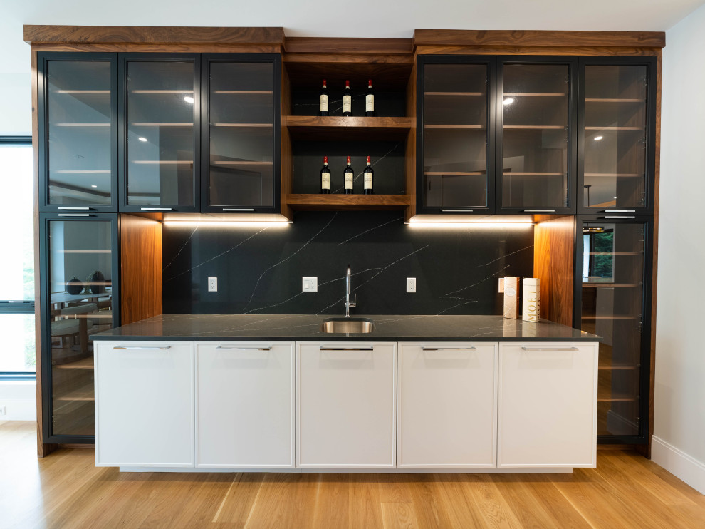 This is an example of a transitional home bar in Boston with an undermount sink, shaker cabinets, quartz benchtops, black splashback, engineered quartz splashback, medium hardwood floors and white benchtop.