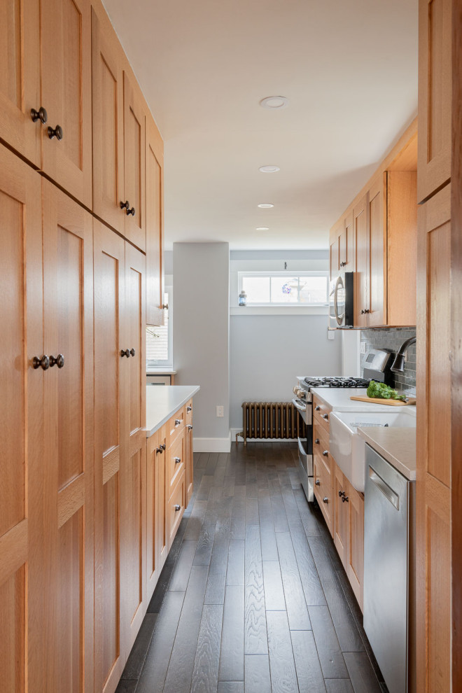 Mid-sized transitional galley medium tone wood floor and brown floor enclosed kitchen photo in Boston with a farmhouse sink, shaker cabinets, light wood cabinets, quartz countertops, gray backsplash, ceramic backsplash, stainless steel appliances and white countertops