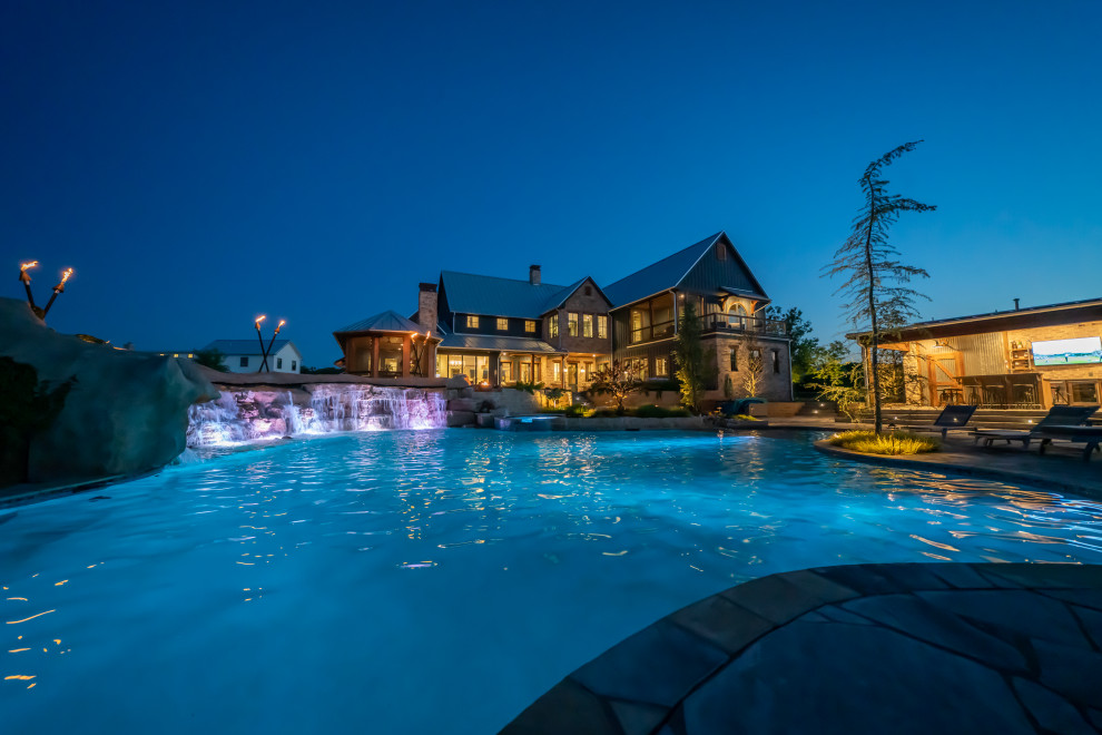 Expansive country backyard custom-shaped natural pool in Oklahoma City with a water feature and natural stone pavers.