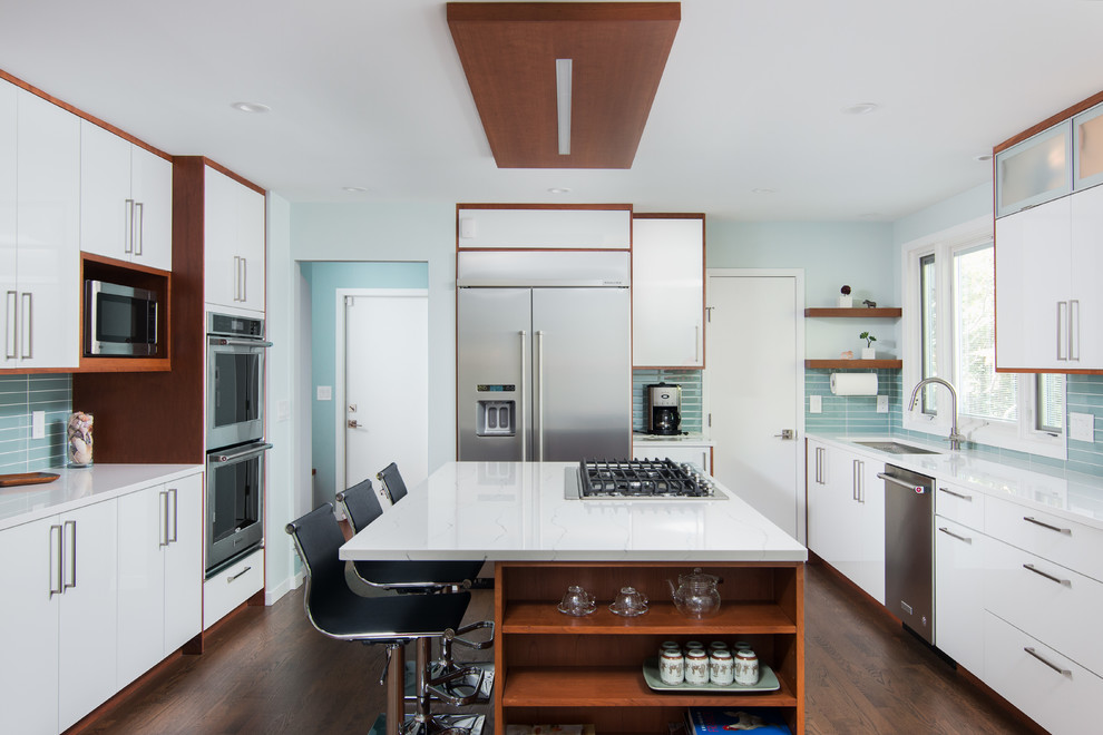 This is an example of a large contemporary u-shaped kitchen in Cleveland with an undermount sink, flat-panel cabinets, white cabinets, blue splashback, glass tile splashback, stainless steel appliances, with island, brown floor, quartz benchtops and dark hardwood floors.