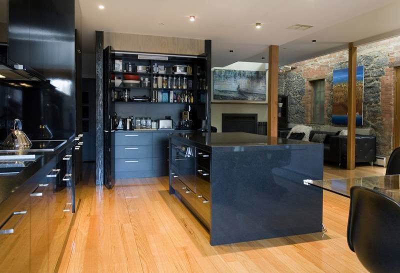 This is an example of a large contemporary galley kitchen pantry in Melbourne with a double-bowl sink, flat-panel cabinets, black cabinets, quartz benchtops, black splashback, glass sheet splashback, panelled appliances, light hardwood floors and with island.