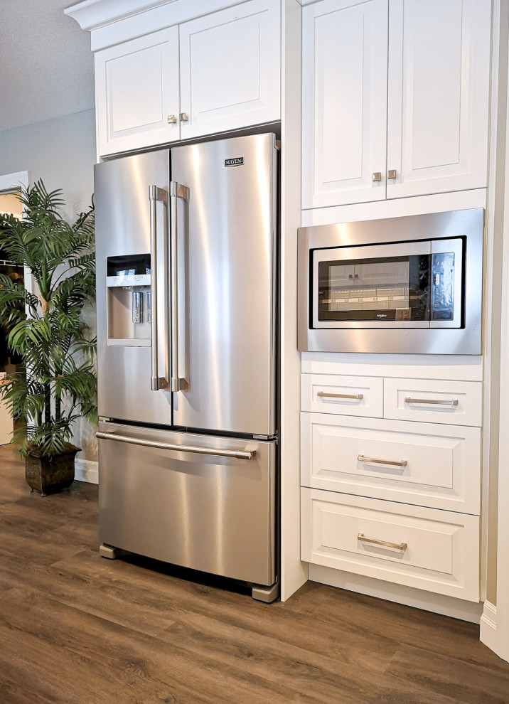 Mid-sized transitional u-shaped light wood floor and brown floor enclosed kitchen photo in Toronto with an undermount sink, raised-panel cabinets, white cabinets, granite countertops, beige backsplash, glass tile backsplash, stainless steel appliances, a peninsula and gray countertops