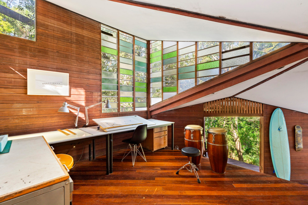 Photo of an expansive midcentury home studio in Brisbane with white walls, dark hardwood floors, a freestanding desk, brown floor, vaulted and wood walls.