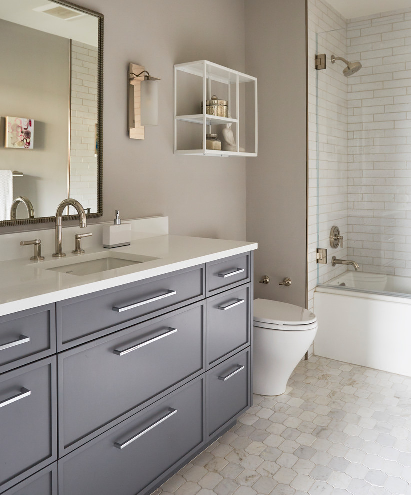 Mid-sized contemporary kids bathroom in Chicago with flat-panel cabinets, grey cabinets, an alcove tub, an alcove shower, a two-piece toilet, white tile, porcelain tile, beige walls, marble floors, an undermount sink, quartzite benchtops, white floor, a hinged shower door and white benchtops.