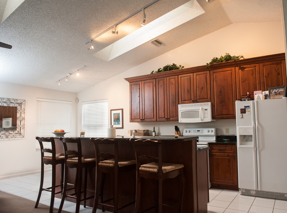 Large transitional galley ceramic tile eat-in kitchen photo in Miami with an undermount sink, dark wood cabinets, granite countertops, white backsplash, white appliances, no island and raised-panel cabinets