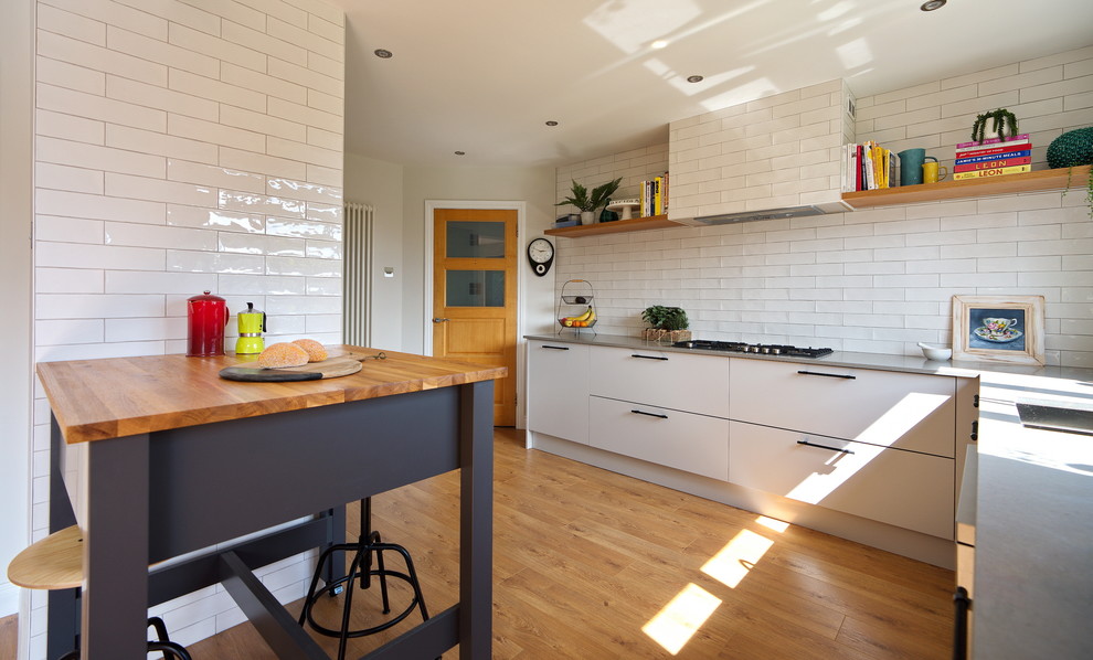 Mid-sized industrial l-shaped eat-in kitchen in Other with a drop-in sink, flat-panel cabinets, grey cabinets, quartzite benchtops, white splashback, ceramic splashback, stainless steel appliances, laminate floors, with island, brown floor and grey benchtop.