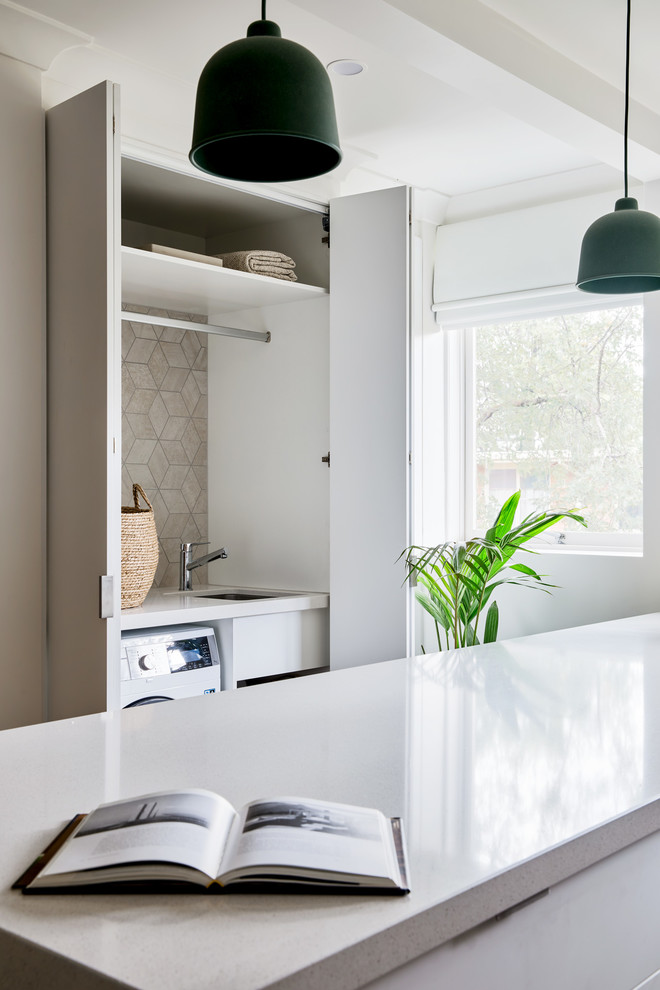 Inspiration for a small contemporary single-wall laundry cupboard in Melbourne with an undermount sink, white cabinets, quartz benchtops, white walls, light hardwood floors, a side-by-side washer and dryer, brown floor and white benchtop.
