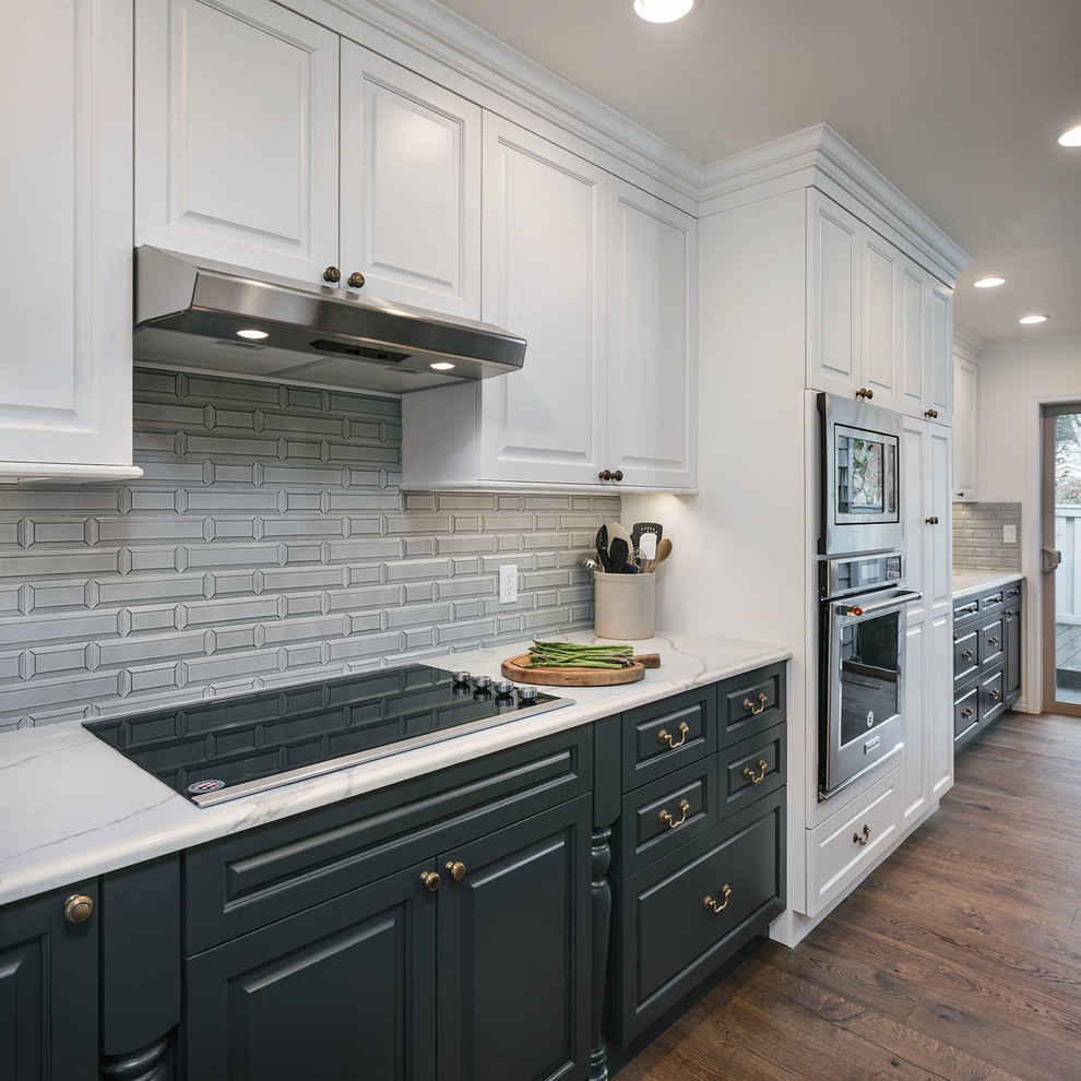 This is an example of a mid-sized transitional galley eat-in kitchen in Portland with a farmhouse sink, raised-panel cabinets, blue cabinets, quartz benchtops, blue splashback, porcelain splashback, stainless steel appliances, light hardwood floors, a peninsula, brown floor and white benchtop.