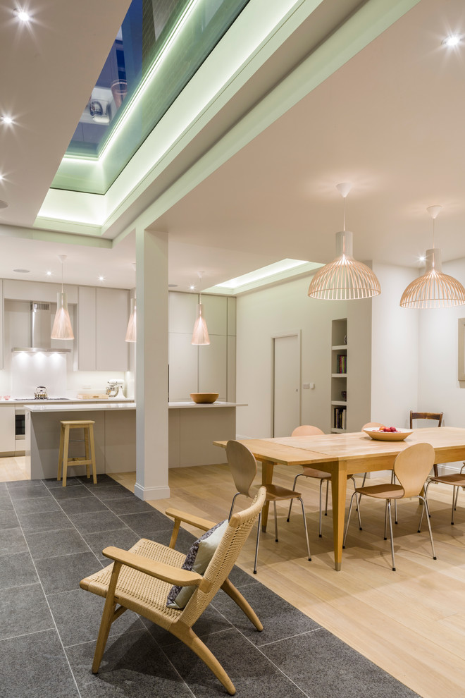 This is an example of a contemporary kitchen/dining combo in London with white walls and light hardwood floors.