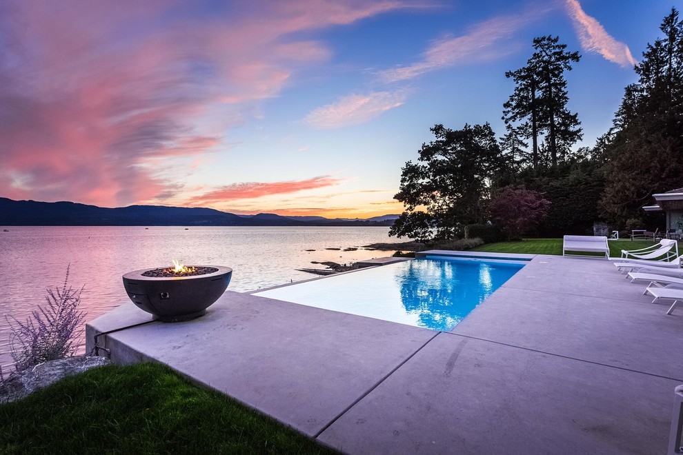Large modern backyard rectangular infinity pool in Vancouver with concrete slab.