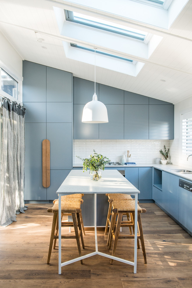 Photo of a beach style kitchen in Sydney with flat-panel cabinets, blue cabinets, white splashback, panelled appliances, dark hardwood floors and with island.