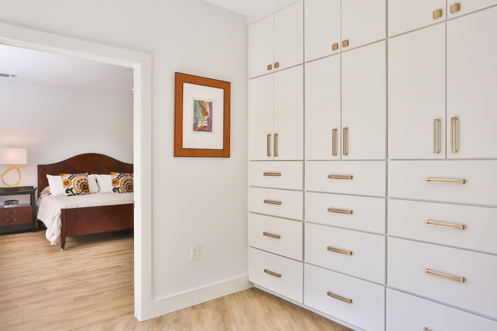Mid-sized midcentury gender-neutral walk-in wardrobe in Austin with flat-panel cabinets, white cabinets, light hardwood floors and beige floor.