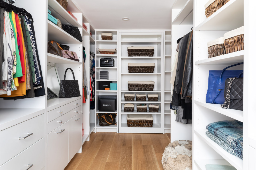 Mid-sized transitional gender-neutral walk-in wardrobe in New York with flat-panel cabinets, white cabinets, light hardwood floors and brown floor.