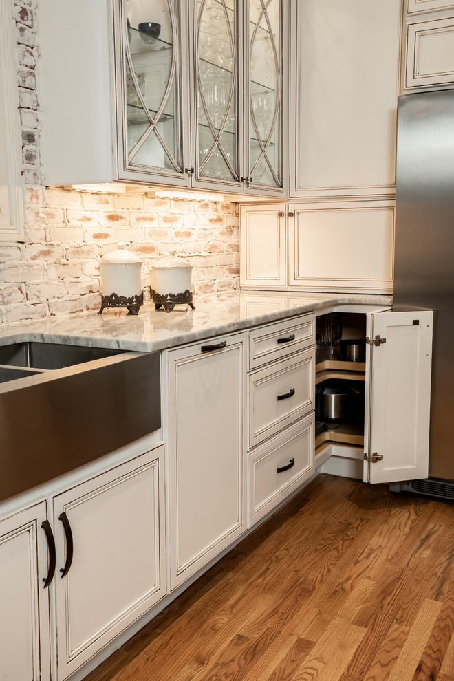 This is an example of a large traditional open plan kitchen in Atlanta with a farmhouse sink, flat-panel cabinets, white cabinets, limestone benchtops, red splashback, brick splashback, stainless steel appliances, light hardwood floors, multiple islands, brown floor and grey benchtop.