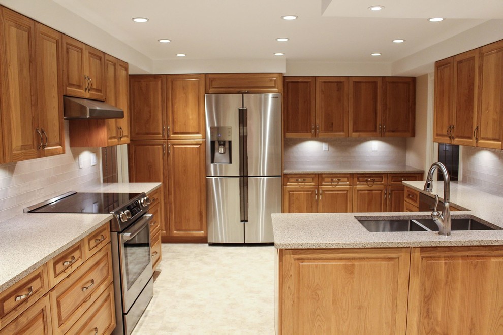 Mid-sized traditional u-shaped separate kitchen in Vancouver with an undermount sink, raised-panel cabinets, medium wood cabinets, quartz benchtops, beige splashback, subway tile splashback, stainless steel appliances, vinyl floors and a peninsula.