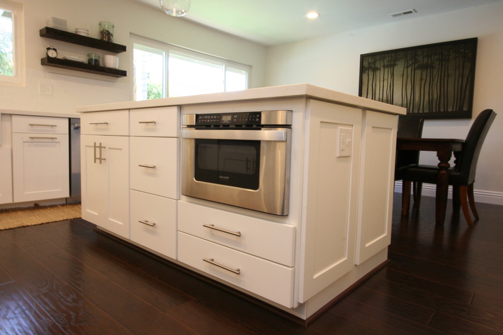 Eat-in kitchen - large transitional u-shaped dark wood floor eat-in kitchen idea in Orange County with a farmhouse sink, shaker cabinets, white cabinets, quartz countertops, white backsplash, ceramic backsplash, stainless steel appliances and an island