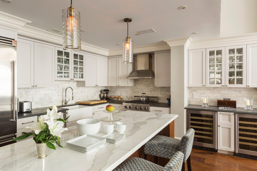 Inspiration for a traditional l-shaped kitchen in New York with a farmhouse sink, glass-front cabinets, white cabinets, marble benchtops, white splashback, marble splashback, stainless steel appliances, medium hardwood floors, with island and orange floor.