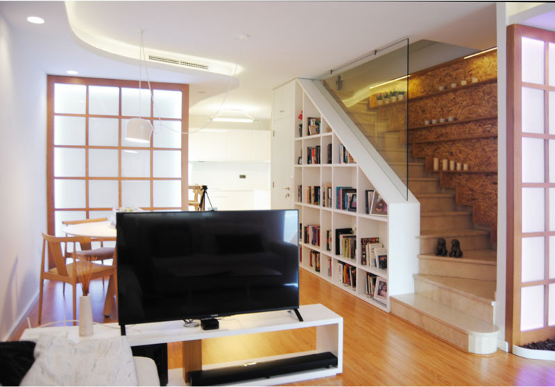 Modelo de sala de estar con biblioteca abierta minimalista pequeña sin chimenea con paredes blancas, suelo de madera en tonos medios, televisor independiente y suelo marrón