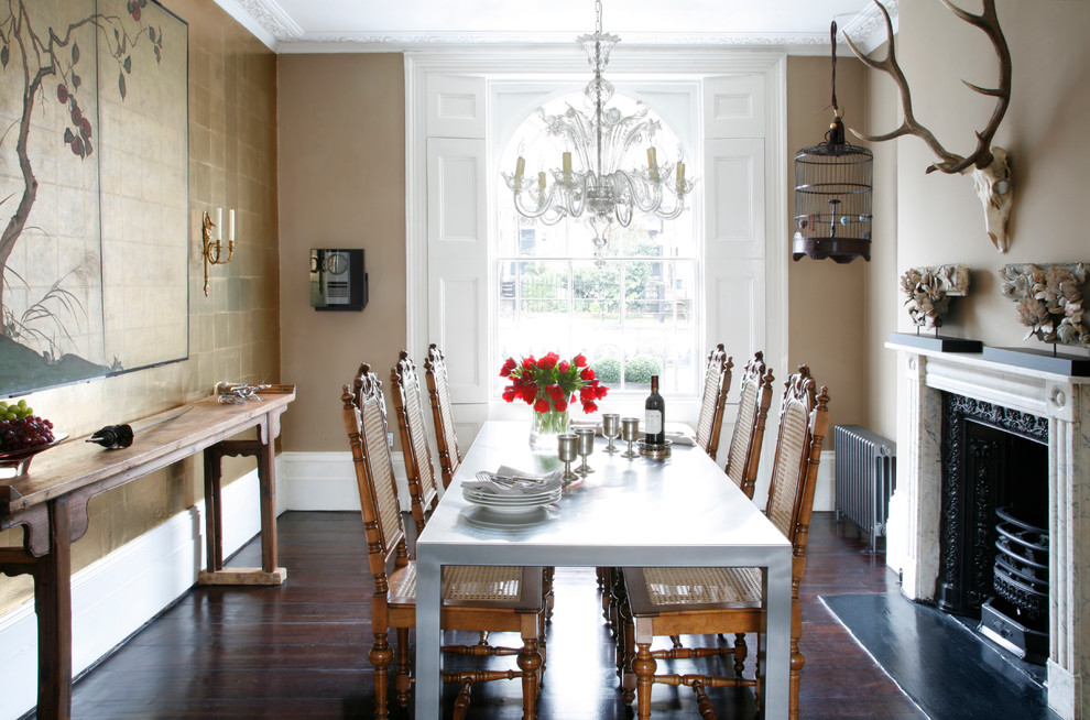 This is an example of an eclectic separate dining room in London with beige walls, dark hardwood floors and a standard fireplace.