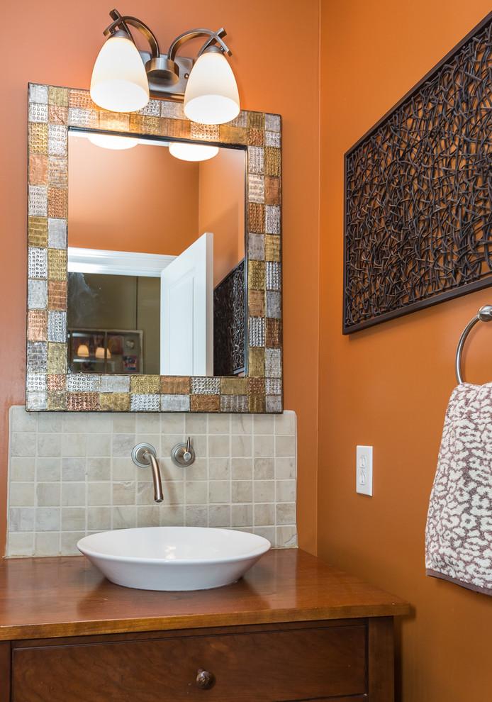 This is an example of a small transitional powder room in Boston with furniture-like cabinets, medium wood cabinets, a two-piece toilet, white tile, stone tile, orange walls, wood benchtops, a vessel sink and brown benchtops.