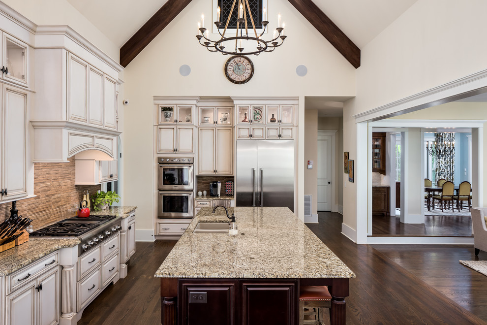 Mid-sized traditional l-shaped eat-in kitchen in Nashville with a double-bowl sink, raised-panel cabinets, beige cabinets, granite benchtops, beige splashback, stone tile splashback, stainless steel appliances, dark hardwood floors and with island.