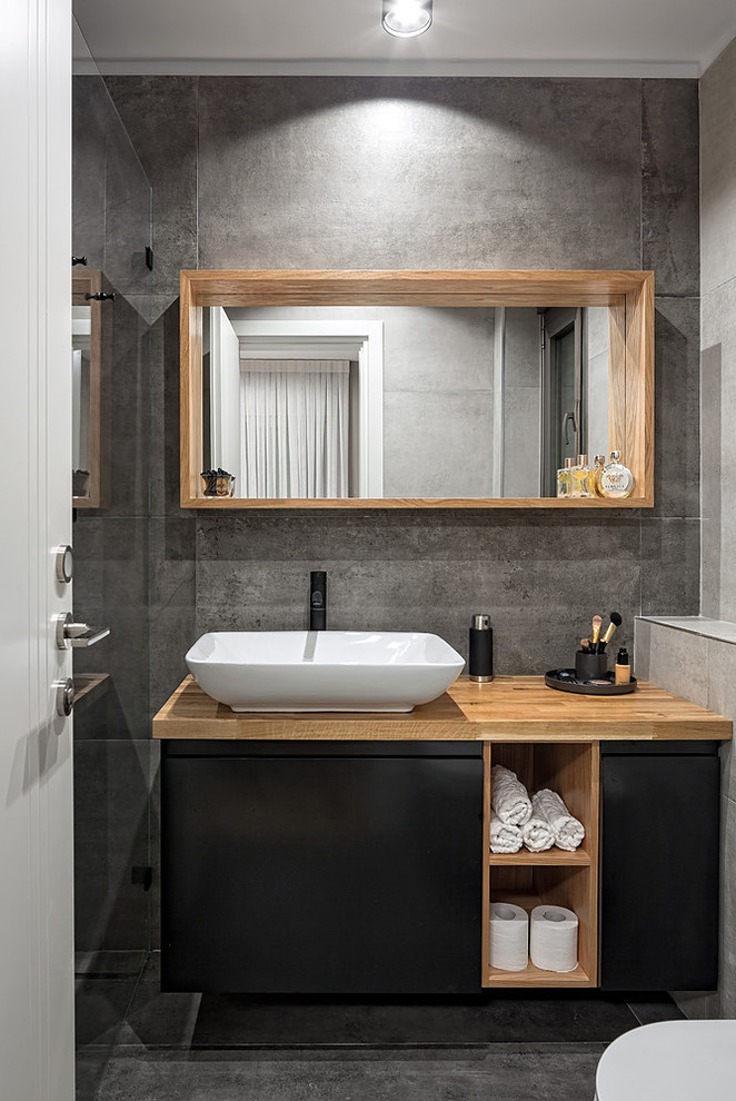 This is an example of a small scandinavian 3/4 bathroom in Tel Aviv with laminate floors, flat-panel cabinets, black cabinets, gray tile, grey walls, a vessel sink, wood benchtops, grey floor and brown benchtops.