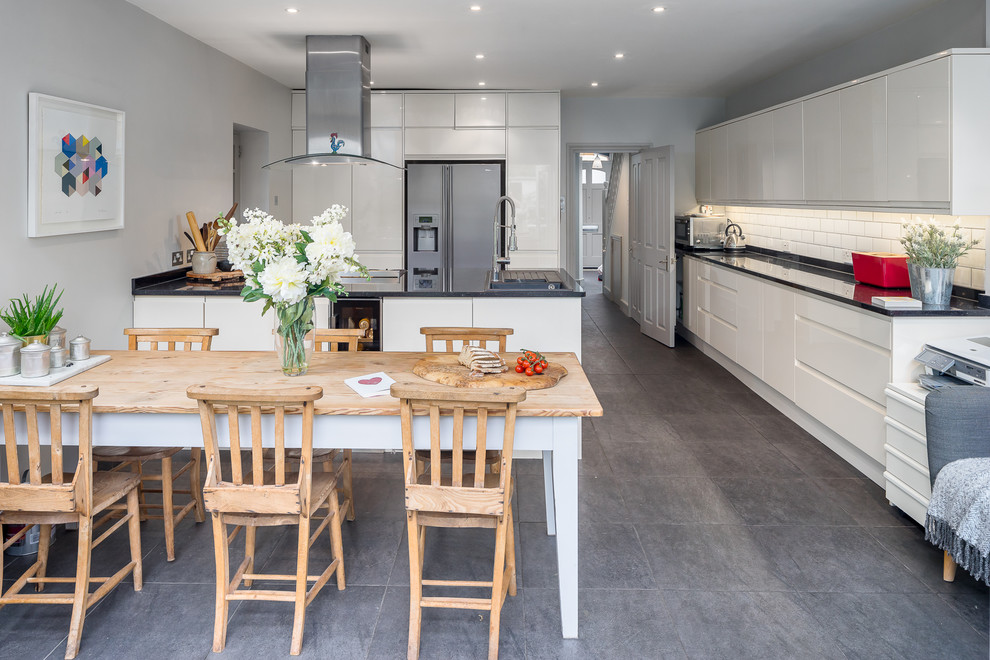 This is an example of a mid-sized contemporary single-wall eat-in kitchen in London with an undermount sink, flat-panel cabinets, white splashback, subway tile splashback, grey floor and black benchtop.