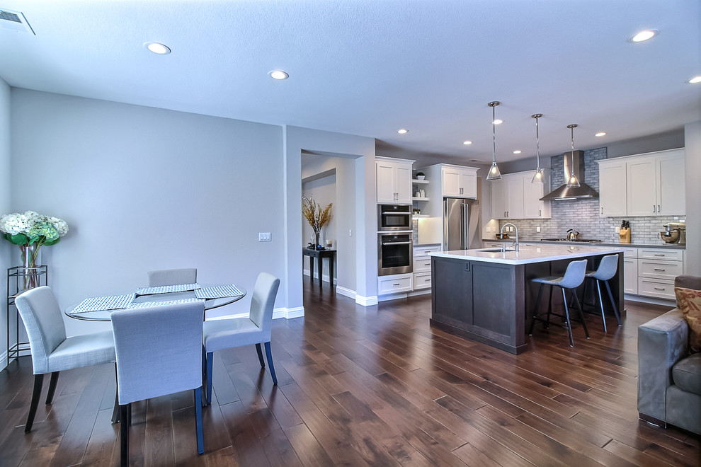 Mid-sized modern l-shaped eat-in kitchen in San Francisco with a single-bowl sink, shaker cabinets, white cabinets, solid surface benchtops, grey splashback, subway tile splashback, stainless steel appliances, medium hardwood floors, with island, brown floor and grey benchtop.