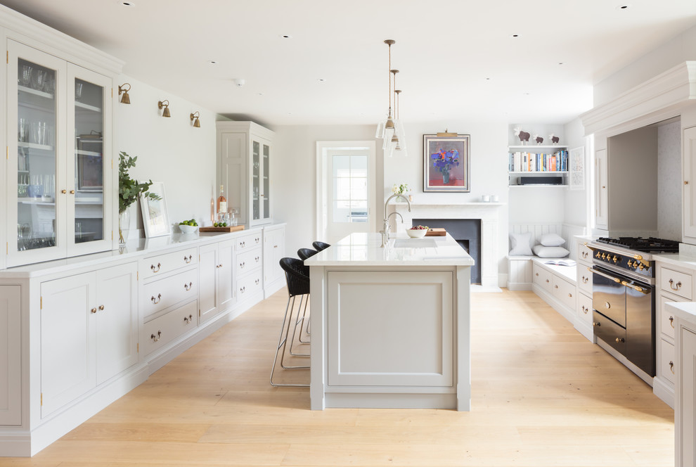 Inspiration for a mid-sized transitional u-shaped kitchen in Hampshire with an integrated sink, shaker cabinets, white cabinets, black appliances, light hardwood floors and with island.