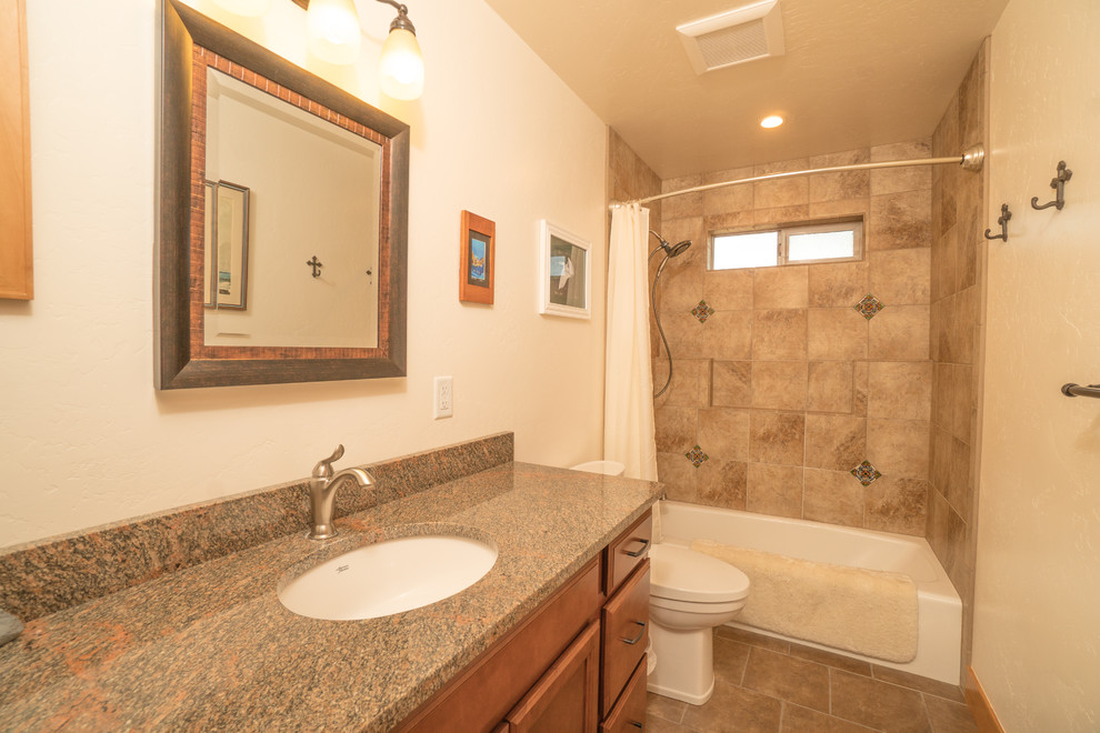 Photo of a mid-sized bathroom in Other with raised-panel cabinets, a shower/bathtub combo, ceramic tile, beige walls, an undermount sink, granite benchtops, brown floor, a shower curtain, multi-coloured benchtops, brown cabinets, a one-piece toilet, beige tile, ceramic floors, a single vanity and a built-in vanity.