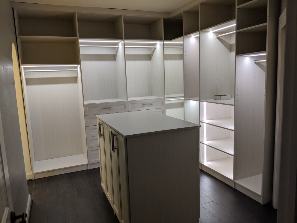 Photo of a mid-sized transitional women's dressing room with glass-front cabinets, light wood cabinets, laminate floors and grey floor.